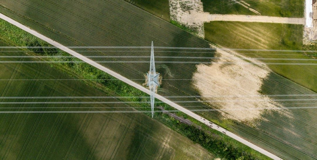 Hochspannungsmast über grünen Feldern und ländlicher Straße aus der Luft